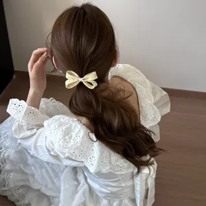 Vue détaillée d'un élastique à cheveux en tissu crème à pois avec un joli nœud papillon