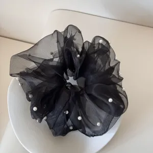 Detailed view of an elegant black mesh scrunchie decorated with white faux pearls