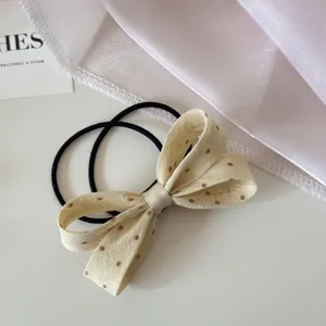 Détail d'un chouchou noeud en tissu à pois beige muni d'un élastique noir haute élasticité.