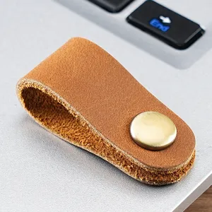 Dettaglio dell'organizer per cavi in pelle marrone con un bottone a pressione in metallo.