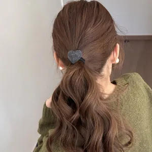 Detail of a plush grey heart-shaped hair tie styling a wavy brown ponytail
