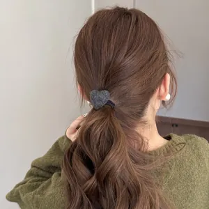 Macro detail of gray plush heart-shaped hair tie worn on a wavy brown hair ponytail