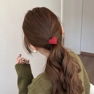 Lifestyle detail of a plush red heart hair tie secured on a model's ponytail, cozy autumn style