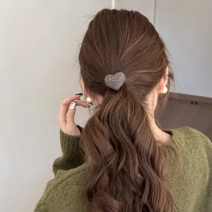 Close-up back view of a model wearing a soft fuzzy plush heart hair tie on a low ponytail