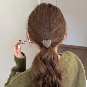 Close-up of a plush grey heart-shaped hair tie worn on a brown ponytail.