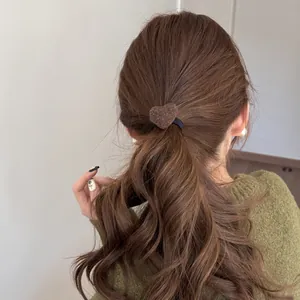 Detail showing a soft brown plush heart hair tie on a low ponytail hairstyle for women.