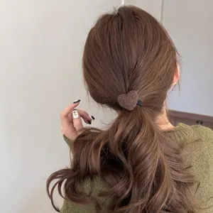 Close-up of a brown fuzzy heart-shaped hair tie on a woman's wavy brown hair.