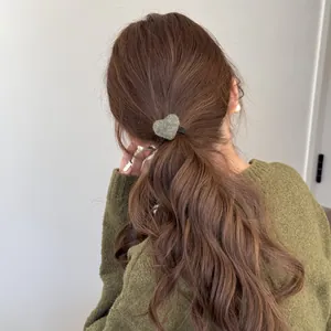 Detailed view of a plush olive green heart-shaped hair tie on a messy low ponytail