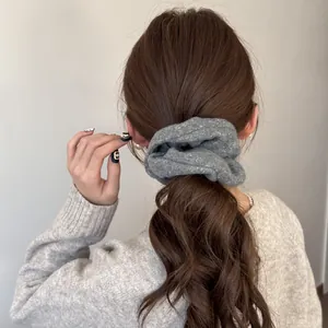 Detail shot of a grey textured felt hair scrunchie worn on a model with a low ponytail