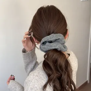 Detail view of a grey felt oversized scrunchie styled in a low ponytail hair look.