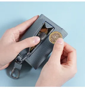 Close-up of coins being put into the zipper pocket of a blue leather key wallet.