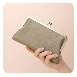 Close-up of a khaki pebbled leather clutch held by a hand to show texture and size.