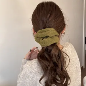 Close-up detail of an olive green fuzzy scrunchie with gold sparkles on a wavy ponytail