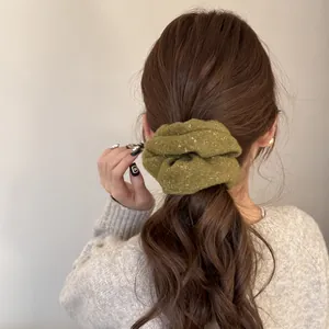 Close-up of green glitter velvet scrunchie styling a low ponytail on brown hair