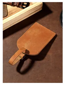 Detail view of a brown crazy horse leather luggage tag on a rustic leather surface.