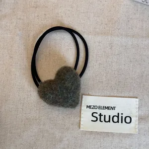 Detail of a plush grey heart-shaped hair tie on a minimalist textured linen background.