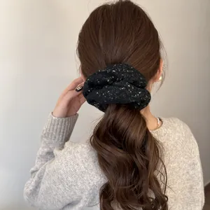 Close-up detail of a soft black plush scrunchie with gold flecks on a wavy ponytail.