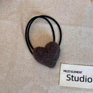 Close-up of a plush brown heart-shaped hair tie on a neutral fabric background