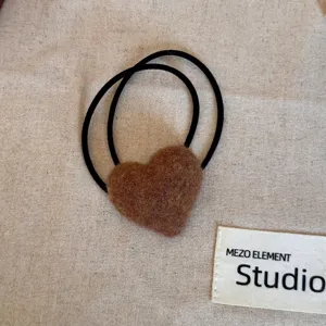 Close-up of a fuzzy brown heart-shaped hair tie on a neutral fabric background