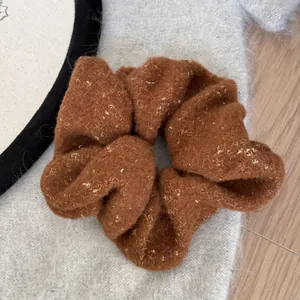 Detail of a brown wool fuzzy scrunchie with shimmering gold metallic thread accents.