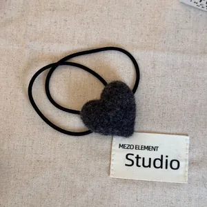 Close-up of black fuzzy heart-shaped hair tie with elastic band on fabric background