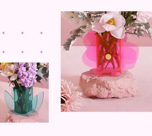 Artistic acrylic flower vases in pink and teal on decorative stones in a studio setting.