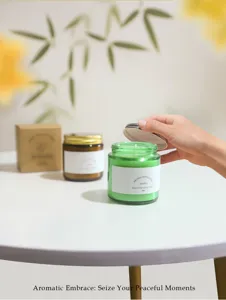 Close-up of opening a green glass jar soy wax scented candle on a white table.