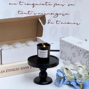 Gros plan d'une bougie parfumée noire en cire de soja sur un socle avec coffret cadeau.