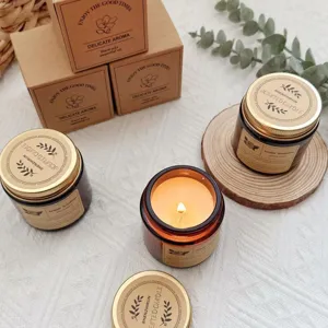 Detailed view of a lit scented soy wax candle in brown glass jar next to kraft gift boxes