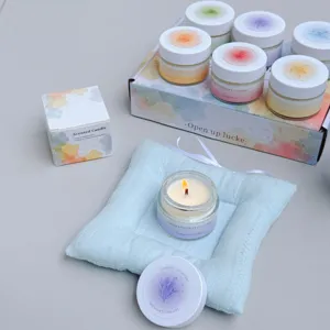 Nahaufnahme einer brennenden Duftkerze auf einem hellblauen Kissen im Geschenkset
