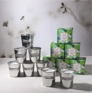 Vista detallada de velas aromáticas en cubos plateados con cajas estampadas de hojas