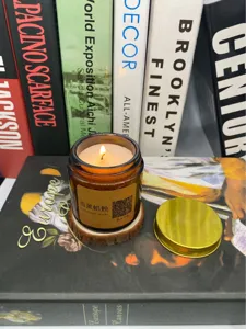 Primer plano de una vela aromática de cera de soja encendida en un frasco de vidrio sobre libros.