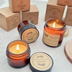 Close-up of amber glass jar scented candles with warm glowing flames and Kraft packaging boxes