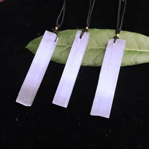 Close-up of three natural selenite bar pendants on a green leaf and black surface