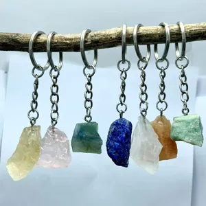 Detailed view of various raw natural crystal keychains hanging from a rustic wooden branch