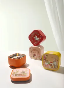 Macro detail of square scented candle tins with cute animal illustrations and lit flame
