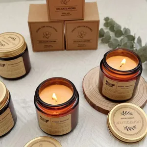 Detail of soy wax candles in brown glass jars with lit flames and gift boxes