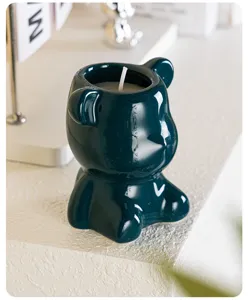 Detail view of a glossy dark teal ceramic bear shaped scented soy wax candle on desk