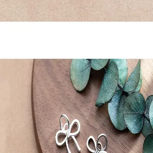 Macro detail of matte S925 silver bow charms displayed on a wooden decorative plate
