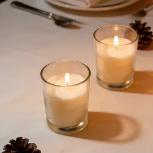 Pair of lit ivory white unscented candles in clear glass cups on a dinner table