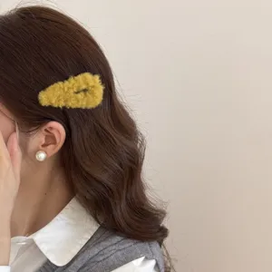 Primer plano de un lindo clip de pelo de peluche amarillo en el cabello castaño ondulado