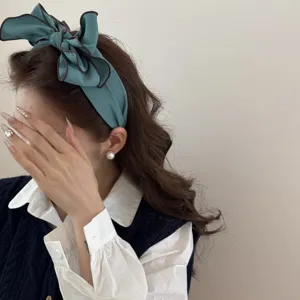 Dettaglio di un cerchietto con fiocco verde acqua e bordi a contrasto su una modella.