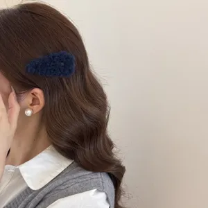 Primer plano de un clip de pelo BB de felpa azul oscuro en el cabello castaño largo y ondulado.