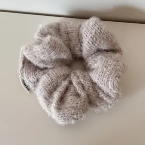 Makro-Detailaufnahme der weichen, flauschigen Strickwolle-Textur dieses beigen Scrunchies