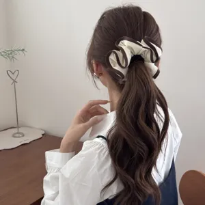 Elegant cream scrunchie with dark brown ruffled trim shown on a wavy ponytail