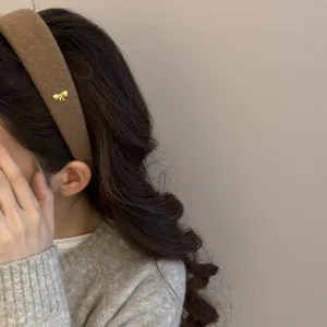 Detalle de una diadema de lana marrón con lazo dorado en una modelo asiática.