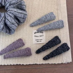 Detailed view of assorted soft woolen hair clips and a scrunchie on a woven mat