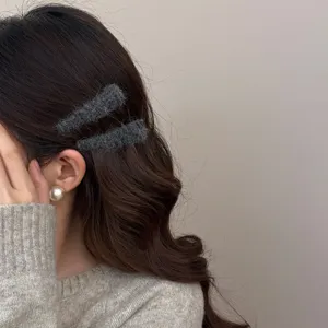 Pair of minimalist dark grey fuzzy woolen BB hair clips styled on wavy dark hair
