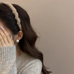 Detalle de la diadema de lana tejida beige y pendiente de perla sobre un modelo