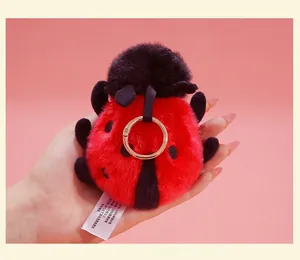 Detailed view of a soft plush ladybug keychain with a golden ring, held by hand.